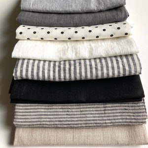 May include: A stack of 10 fabric swatches in various colors and patterns, including black, white, gray, and beige. The fabrics are arranged in a neat pile, with the top swatch being a light beige linen.