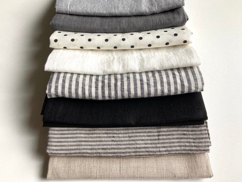 May include: A stack of 10 fabric swatches in various colors and patterns, including black, white, gray, and beige. The fabrics are arranged in a neat pile, with the top swatch being a light beige linen.