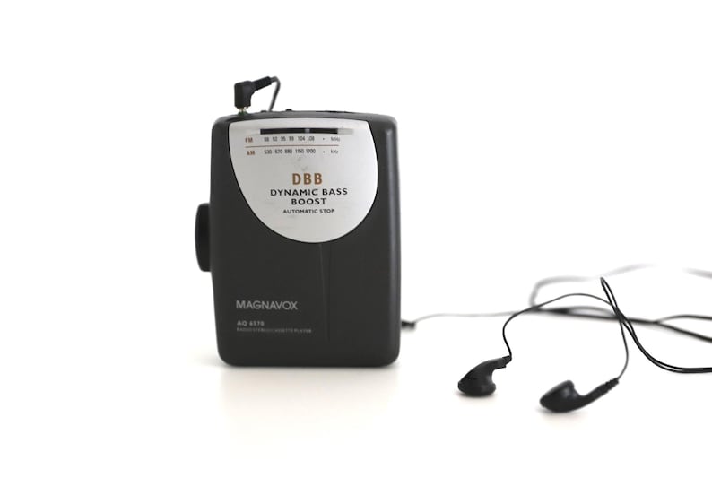 Puede incluir: Un reproductor de casetes port&aacute;til negro y plateado con una antena incorporada y una toma de auriculares. El reproductor tiene el texto "DBB DYNAMIC BASS BOOST AUTOMATIC STOP" y "MAGNAVOX" impreso en &eacute;l. El reproductor est&aacute; conectado a un par de auriculares de bot&oacute;n negros.