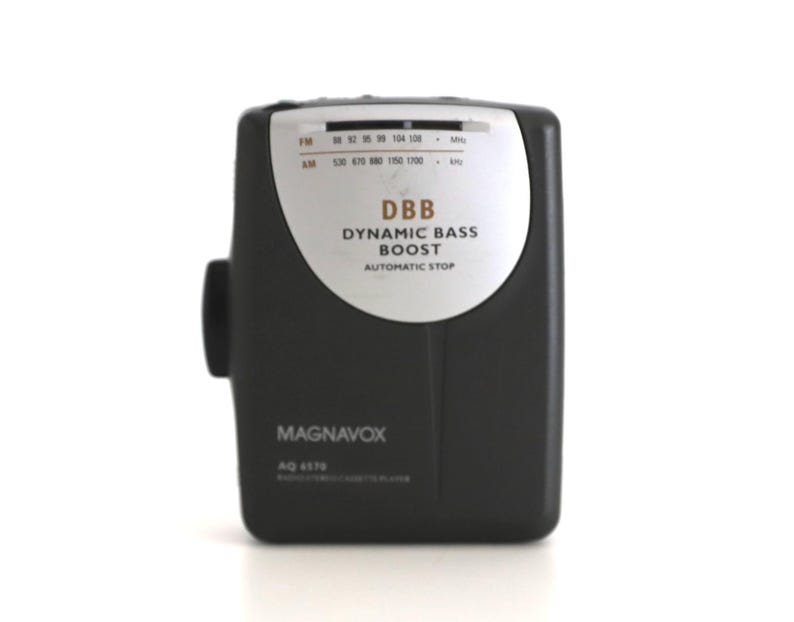 Puede incluir: Un reproductor de casetes port&aacute;til negro y plateado con el texto "DBB Dynamic Bass Boost Automatic Stop" y "MAGNAVOX AQ 1570" en la parte delantera.