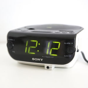 May include: A black and white Sony CD clock radio with a green digital display showing 12:12. The radio has buttons for alarm A, alarm B, and audio in.