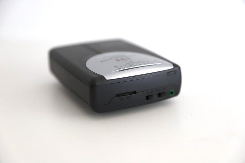 Puede incluir: Un reproductor de casetes negro y plateado con una toma de auriculares y una perilla de control de volumen.