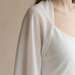 May include: A white, sheer, long-sleeved garment with a square neckline. The fabric is lightweight and appears to drape softly. The garment is likely a top or a dress overlay.