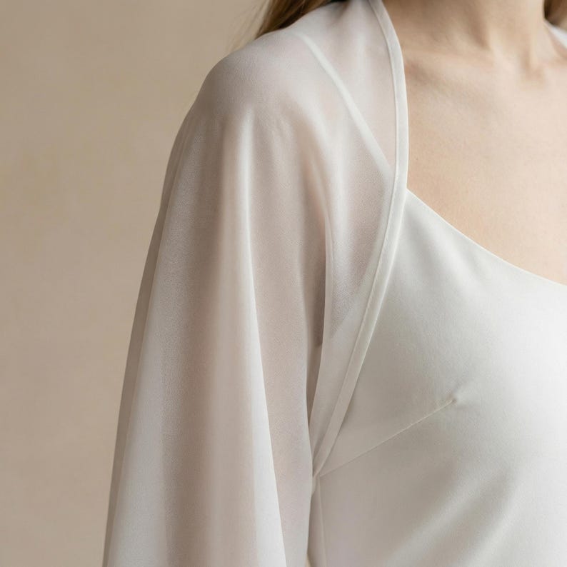 May include: A white, sheer, long-sleeved garment with a square neckline. The fabric is lightweight and appears to drape softly. The garment is likely a top or a dress overlay.