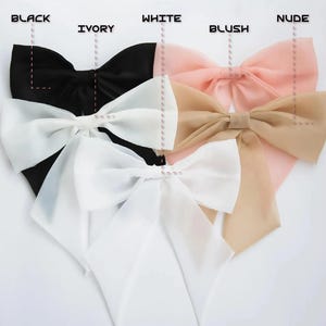 May include: A collection of large, elegant bows in various colors, including black, ivory, white, blush, and nude. Each bow is made of a delicate, sheer fabric and features a decorative center.