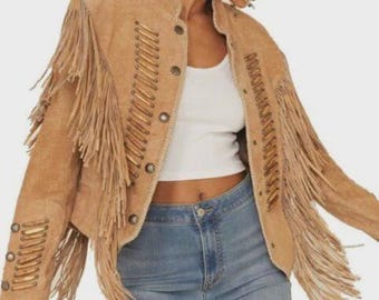 May include: A tan suede jacket with long fringe detailing on the sleeves and chest. The jacket features decorative stitching and button closures. The jacket is worn with a white top and blue jeans.