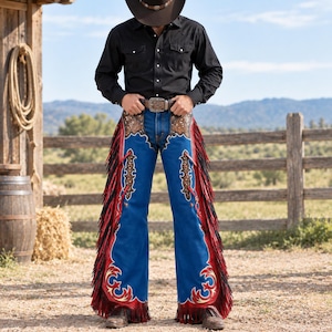 May include: A pair of blue leather chaps featuring red leather trim, black fringe along the sides, and intricate brown floral tooling on the upper sections. The chaps are worn over blue denim jeans, paired with a black long-sleeve shirt and a brown hat.