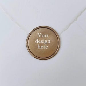 May include: A round, bronze-colored wax seal with the text "Your design here" in white. The seal is set against a white background, suggesting stationery or packaging. The design is simple and elegant, suitable for various applications.