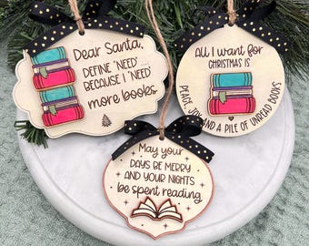 May include: Three wooden Christmas ornaments with black and gold polka dot ribbons. One ornament says "Dear Santa, define 'need' because I 'need' more books." Another says "All I want for Christmas is a pile of unread books."