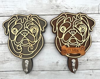 May include: Two wooden pug-shaped wall hooks. One is dark brown, the other is medium brown, both with a light brown outline. The medium brown hook has a bone-shaped tag that says "OLIVER". Each hook has a silver-colored metal hook.