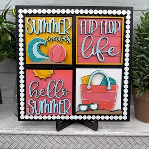 May include: A decorative wooden sign with a black frame and white dot border. The sign features four colorful panels with summer-themed text and images, including waves, a beach ball, and a beach bag. The words "Summer", "Flip Flop", and "Hello Summer" are visible.