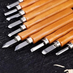 May include: A set of 10 wood carving tools with brown wooden handles and silver metal blades. The tools are arranged in a row on a black surface.