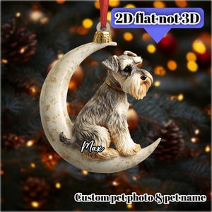 Può includere: Un ornamento decorativo con un cane Schnauzer seduto su una luna crescente. L'ornamento ha una parte superiore color oro e un nastro rosso per appenderlo. Il testo "Max" è scritto sulla luna e il testo "Custom pet photo & pet name" è in basso.