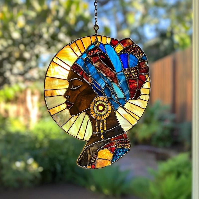 May include: Stained glass panel depicting a woman's profile with a colorful head wrap and earrings. The panel features shades of blue, red, yellow, and brown, with a circular halo design. The artwork is suspended by a chain.