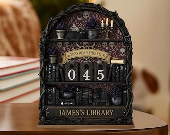 May include: A decorative bookshelf-shaped calendar with a gothic theme. The black frame features a shelf design with miniature books, plants, and a black cat figurine. The calendar displays the numbers "045" and the text "Books Read This Year" and "James's Library".