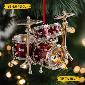 May include: A red and gold drum kit Christmas ornament with the name "Martin" on the bass drum. The ornament has a red ribbon for hanging and the text "2D FLAT NOT 3D" and "CUSTOM NAME" in yellow.
