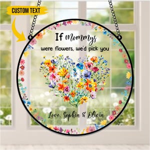 Puede incluir: Un letrero redondo de vidrio transparente con borde negro, con un arreglo floral en forma de corazón en colores vibrantes. El texto dice "If Mommys were flowers, we'd pick you" y "Love, Sophia & Olivia". Cuelga de una cadena.