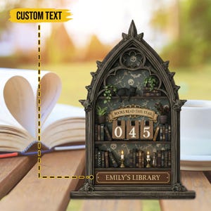 May include: A gothic-style bookshelf with the text "BOOKS READ THIS YEAR" and the number "045". The shelf features miniature books, plants, a black cat, and candles. The bottom of the shelf reads "EMILY'S LIBRARY".