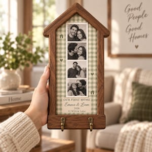 Può includere: Una targa da parete in legno a forma di casa con una striscia verticale di quattro foto in bianco e nero di una coppia. Lo sfondo presenta un motivo a quadretti verde salvia con icone di case e cuori. Il testo recita: OUR FIRST HOME, Emma & Liam, 2026, 12 Willow Lane. Due ganci in ottone sono fissati nella parte inferiore.