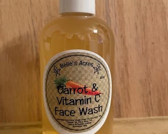 May include: A clear glass bottle with a white cap containing a yellow liquid. The bottle has a white label with the text "Belle's Acres Carrot & Vitamin C Face Wash" and a list of ingredients.