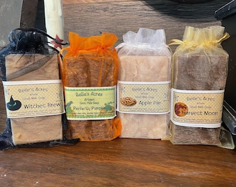 May include: Four rectangular bars of Belle's Acres artisan goat milk soap, each individually wrapped in sheer organza drawstring bags in black, orange, white, and gold. The labels feature the names Witches Brew, Perfectly Pumpkin, Apple Pie, and Harvest Moon.