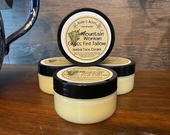 May include: Three round jars of Belle's Acres Handmade Mountain Woman Grass Fed Tallow Herbal Face Cream. Each jar has a black lid and a cream-colored label with black text and a small green plant illustration. The jars contain a pale yellow cream.