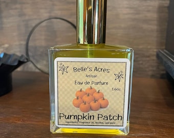May include: A rectangular glass perfume bottle with a gold cap containing yellow liquid. The label reads Belle's Acres Artisan Eau de Parfum 1.6oz Pumpkin Patch with an illustration of small pumpkins and a list of ingredients including fragrance oil.