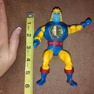 Puede incluir: Figura de acción vintage de un personaje humanoide, principalmente azul y amarillo, con detalles rojos. La figura tiene un emblema similar a un radar en el pecho y mide aproximadamente 13 cm de alto. Juguete coleccionable.