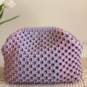 Pode incluir: Bolsa de mão de macramé atada à mão em tons de lavanda e roxo. A bolsa tecida apresenta um padrão geométrico e uma forma arredondada. Feita de cordão de algodão macio, ideal para transportar o essencial. Aproximadamente 30 cm de largura.