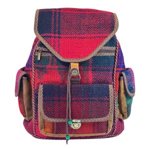 Peut inclure: Un sac à dos en tissu à carreaux rouge, noir et vert avec des accents en cuir marron et une poche zippée à l'avant. Le sac à dos a une fermeture à cordon et une petite poche sur le devant.