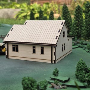 May include: A miniature wooden house with a light-colored exterior and a contrasting dark brown roof and trim. The model has multiple windows and is set on a green surface with miniature trees and a yellow toy vehicle. The house is a detailed architectural model.