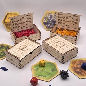 May include: Wooden Catan board game set with resource tokens, dice, and hexagonal game tiles. The set includes wooden boxes with the word "CATAN" on the lids. The game pieces are in various colors, including red, yellow, and blue.