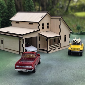 May include: A miniature wooden house with a garage, a red Chevrolet pickup truck, a white car in the garage, and a yellow Jeep toy. The house has a light wood finish with black trim. The scene is set on a green surface.