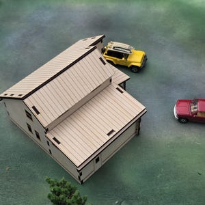May include: A miniature wooden house with a light brown finish, featuring a sloped roof and rectangular windows. A yellow toy SUV with a surfboard and a red pickup truck are nearby. The scene is set on a green surface.