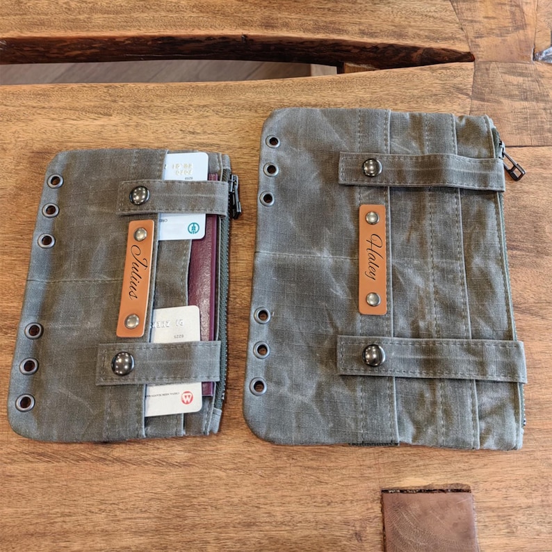 Op de afbeelding: Twee olijfgroene canvas portemonnees met leren details en metalen ogen. E&eacute;n portemonnee is open en toont kaarten en een paspoort. De andere heeft een ritssluiting. Beide hebben een leren label met een naam.