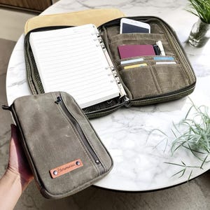 May include: A green canvas organizer with a zippered closure, open to reveal a notebook and pockets for a phone, cards, and pens. A smaller matching pouch with the name "Hermosa" is also visible.