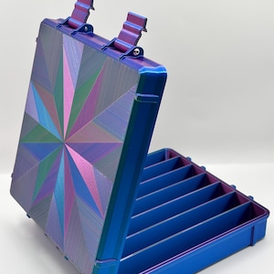 May include: A rectangular storage case with a hinged lid featuring a multi-colored iridescent starburst pattern in shades of blue, purple, and green. The interior of the case is divided into six parallel compartments, and the exterior is blue.