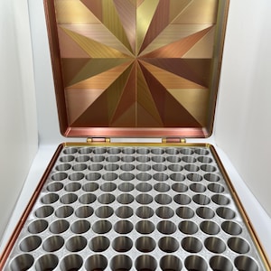 以下が含まれることがあります： 蓋に幾何学模様が施された、金色と銅色の収納ボックス。ボックスには、100個の丸い仕切りが付いた取り外し可能なトレイが付いています。