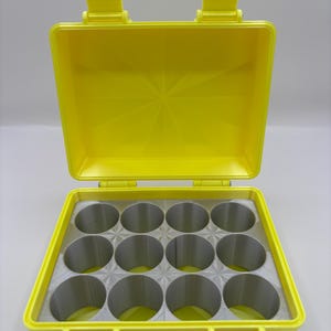 May include: Bright yellow plastic case with an open lid. The interior features a gray foam insert with twelve circular compartments. The case has a handle and two latches for secure closure. The case is designed to hold small cylindrical objects.