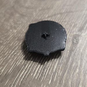 Może przedstawiać: Czarny plastikowy przedmiot wydrukowany w 3D o okrągłym kształcie z małym otworem w środku.