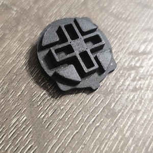 Może przedstawiać: Czarny, plastikowy przedmiot wydrukowany w 3D z geometrycznym wzorem. Przedmiot ma okrągły kształt z krzyżowym wzorem w środku.