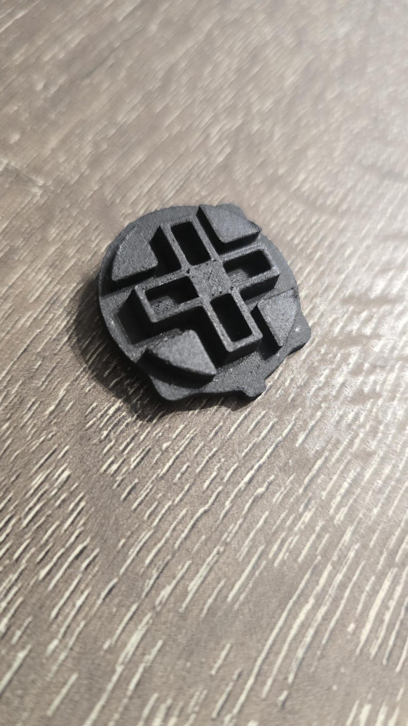 Może przedstawiać: Czarny, plastikowy przedmiot wydrukowany w 3D z geometrycznym wzorem. Przedmiot ma okrągły kształt z krzyżowym wzorem w środku.