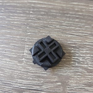Może przedstawiać: Czarna plastikowa nakrętka z krzyżowym wzorem. Nakrętka jest zaprojektowana do dopasowania do śruby lub śruby.