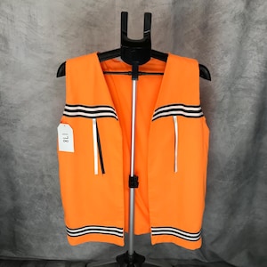 May include: Bright orange vest with black and white stripes. The vest has a simple design with a high visibility color. The vest is hanging on a black hanger.