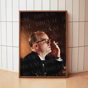 May include: A framed portrait of a man in a suit, wearing glasses, and smoking a cigarette. The background features a repeating pattern of the word "DRUVAL". The image is in a brown wooden frame.