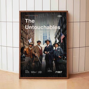 Puede incluir: Un póster enmarcado de la película "Los Intocables" con cuatro hombres con trajes y sombreros, sosteniendo armas, en una calle. El póster incluye el título de la película, los créditos y el año 1987.