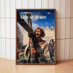 以下が含まれることがあります： 「Life of Brain」と「/1979」の文字が入った額縁入りのポスター。青い空と古代建築を背景に、男性が木の十字架を運んでいる様子が描かれています。ポスターは茶色の木製フレームに入っています。