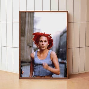Könnte beinhalten: Gerahmter Druck, der eine Frau mit leuchtend roten Haaren zeigt, die in einer Stadt läuft. Sie trägt ein blaues Tanktop. Der Druck befindet sich in einem braunen Holzrahmen, der vor einer weißen gefliesten Wand präsentiert wird.