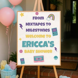 Könnte beinhalten: Eine Holzstaffelei zeigt ein Babyparty-Schild mit dem Text "From Mixtapes to Milestones Welcome to Ericca's Baby Shower". Das Schild ist mit Retro-Grafiken verziert. Rosa und blaue Luftballons, ein Teddybär und Geschenkboxen sind in der Nähe.