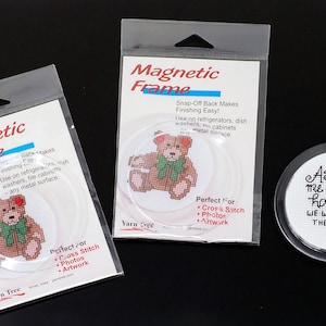 May include: Two clear plastic frames with magnetic backs for displaying cross stitch, photos, or artwork. The frames are packaged in clear plastic bags with the text "Magnetic Frame" printed on the front. The frames are shown with a cross stitch of a teddy bear and a cross stitch with the text "As for me and my house - we will serve the Lord".
